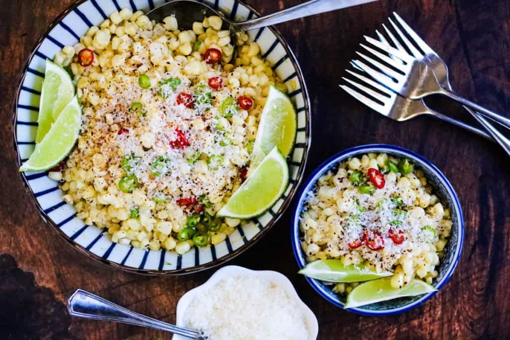 Mexican corn salad with limes, jalapeños, and cheese in bowls ready to eat