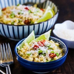 Two bowls of Mexican corn salad with lime and parmesan on a wooden table.