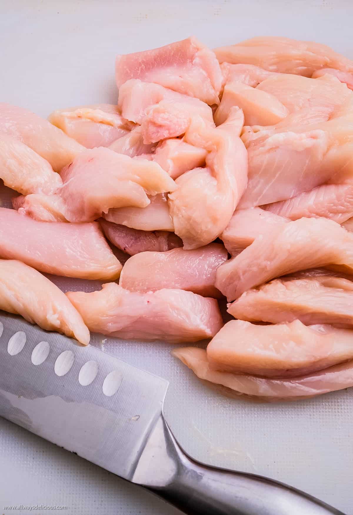 Cut chicken breasts on a cutting board to prepare chicken satay.