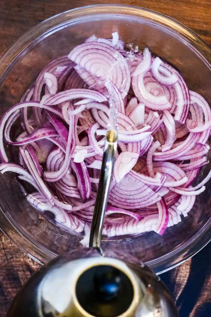 Pouring hot water over sliced red onions for making mexican pickled onions.