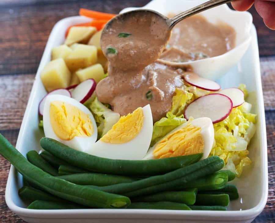 spooning thai peanut sauce onto gado gado salad