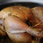 A roast chicken is being cooked in a pan with herbs.