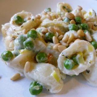 A white plate with orecchiette, peas, and pine nuts.
