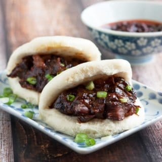 Two char siu bao on a plate next to a bowl of sauce.