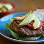 A turkey burger topped with avocado and tomatoes on a blue plate.