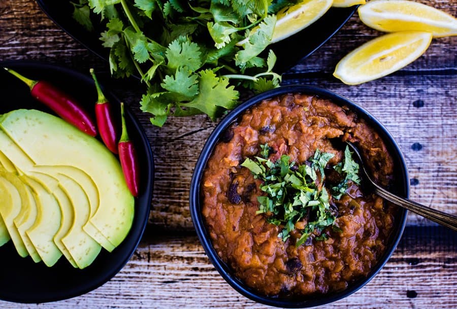 A bowl of vegetarian black bean chili with avocado and lime on a wooden table.