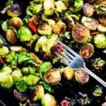 Overhead shot of a skillet of pan-seared brussels sprouts with red chiles. There is a fork picking up a sprout.