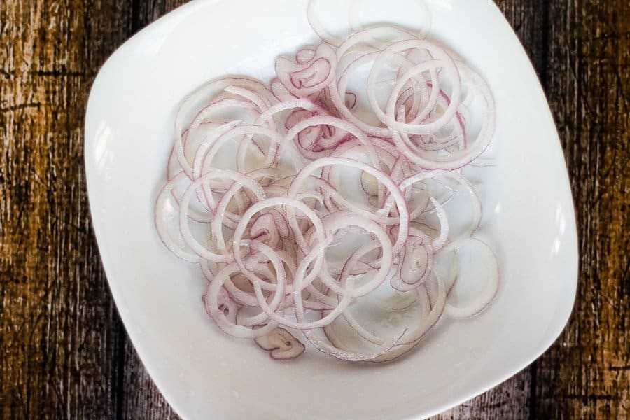 Sliced shallots in a microwave-safe bowl tossed with cooking oil