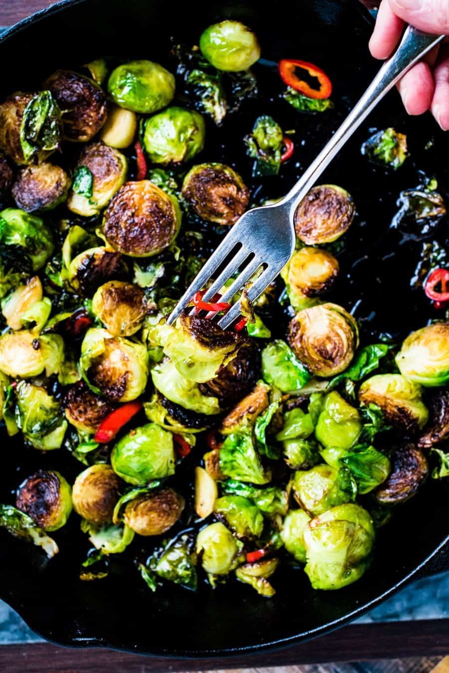 Overhead shot of a skillet of pan-seared brussels sprouts with red chiles. There is a fork picking up a sprout.