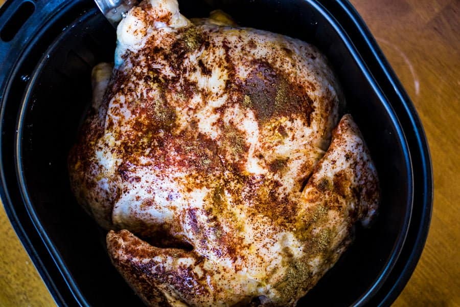 whole chicken rubbed with spices in the air fryer basket ready to be cooked