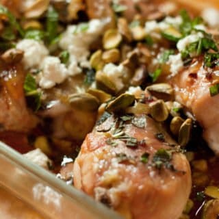Roasted lemon chicken with feta and pine nuts in a baking dish.