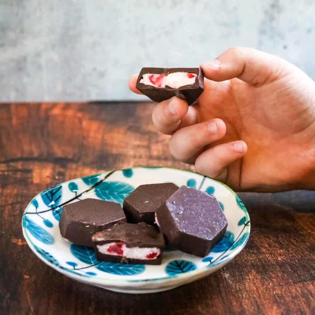 chocolate-covered strawberry cheesecake bites on a plate and one in hand