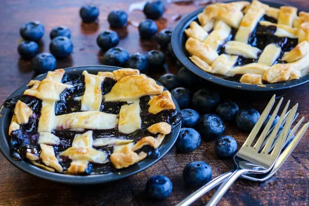 Mini blueberry pie with two forks and lots of fresh blueberries