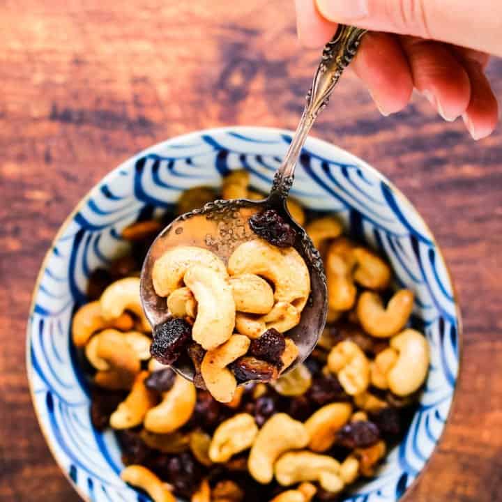 Caramelized cashews and raisins in a bowl with a silver spoon being lifted