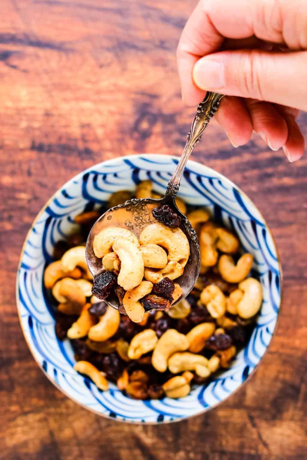 Caramelized cashews and raisins in a bowl with a silver spoon being lifted