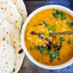 A bowl of mulligatawny soup with a spoon next to a plate of naan.