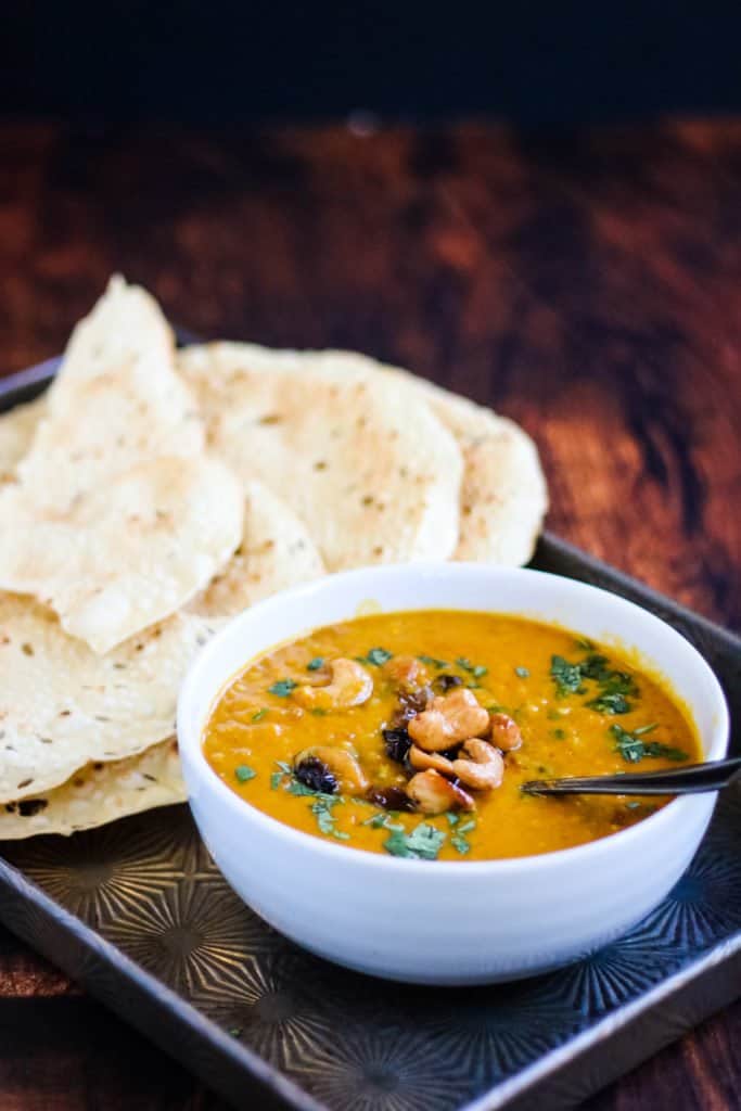 instant pot mulligatawny soup in a bowl on a metal tray with papadums on the side.