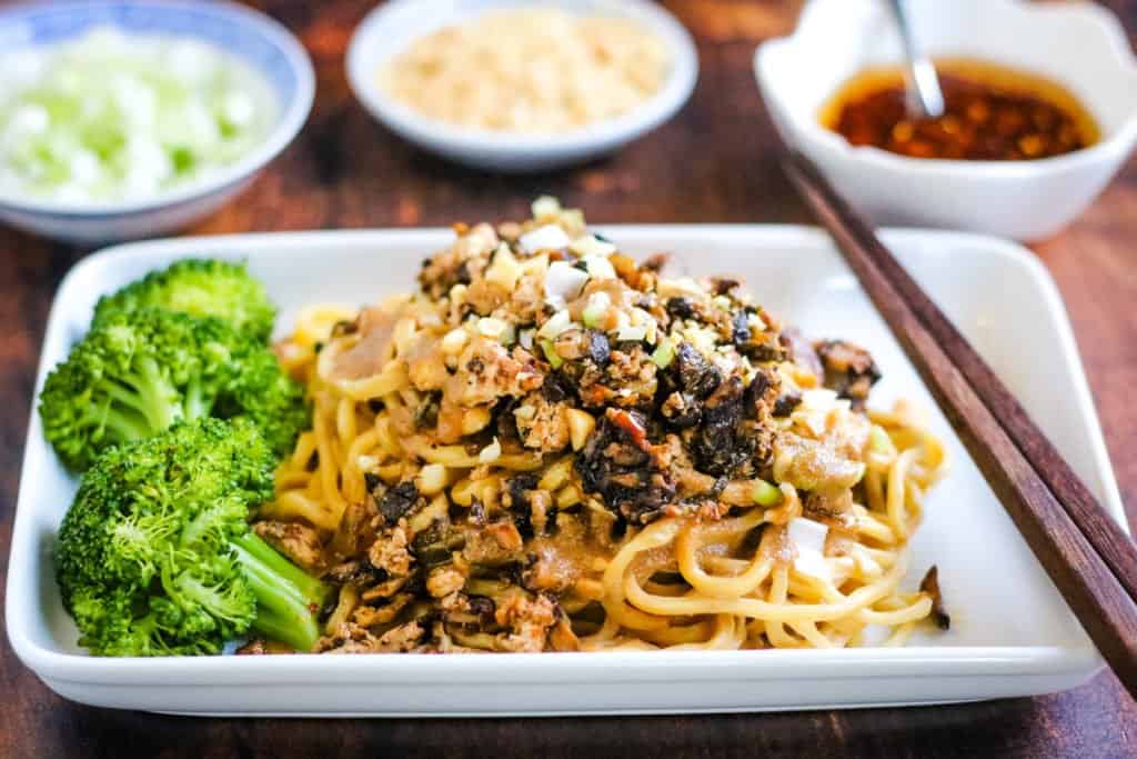 Vegetarian dan dan noodles ready to eat on a plate with broccoli.