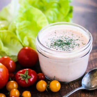 A jar of Sriracha ranch dressing with tomatoes and lettuce.