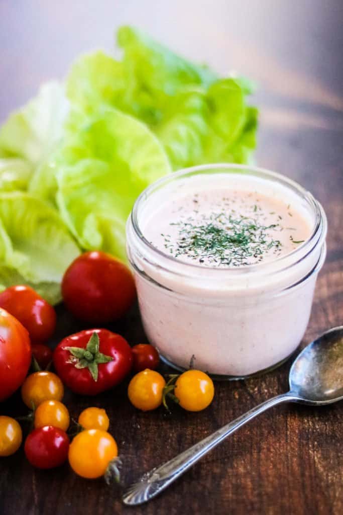 sriracha ranch dressing in a jar with tomatoes and lettuce and a spoon on a wood table