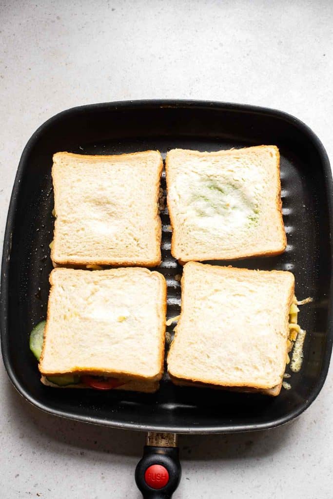 A frying pan with four uncooked Bombay Sandwiches on it.