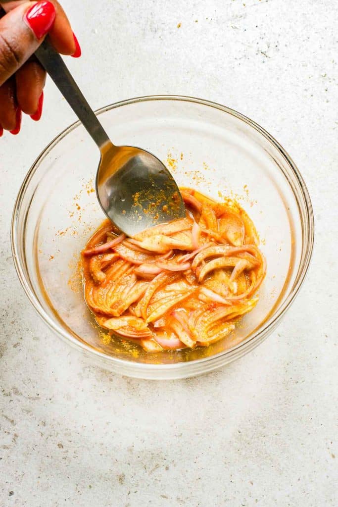 A person stirring spiced onions in a bowl with a spoon.