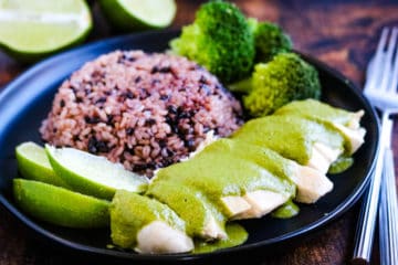 Thai green curry chicken on a plate with multi-grain purple rice, broccoli. and lime wedges