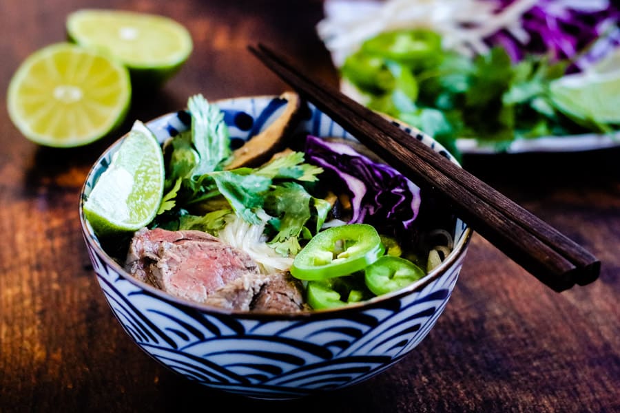 instant pot beef pho in a bowl garnished with cilantro, lime wedges, chile slices, and bean sprouts