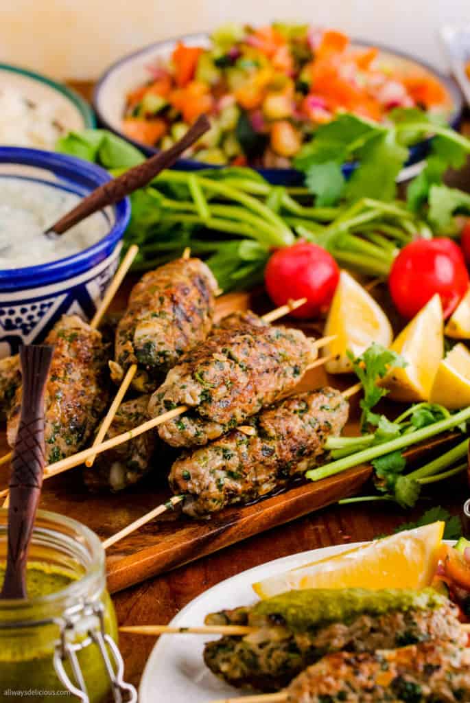 low angle shot of lamb kofta kebabs on a platter with radishes, lemon wedges, herbs, and tzatziki.