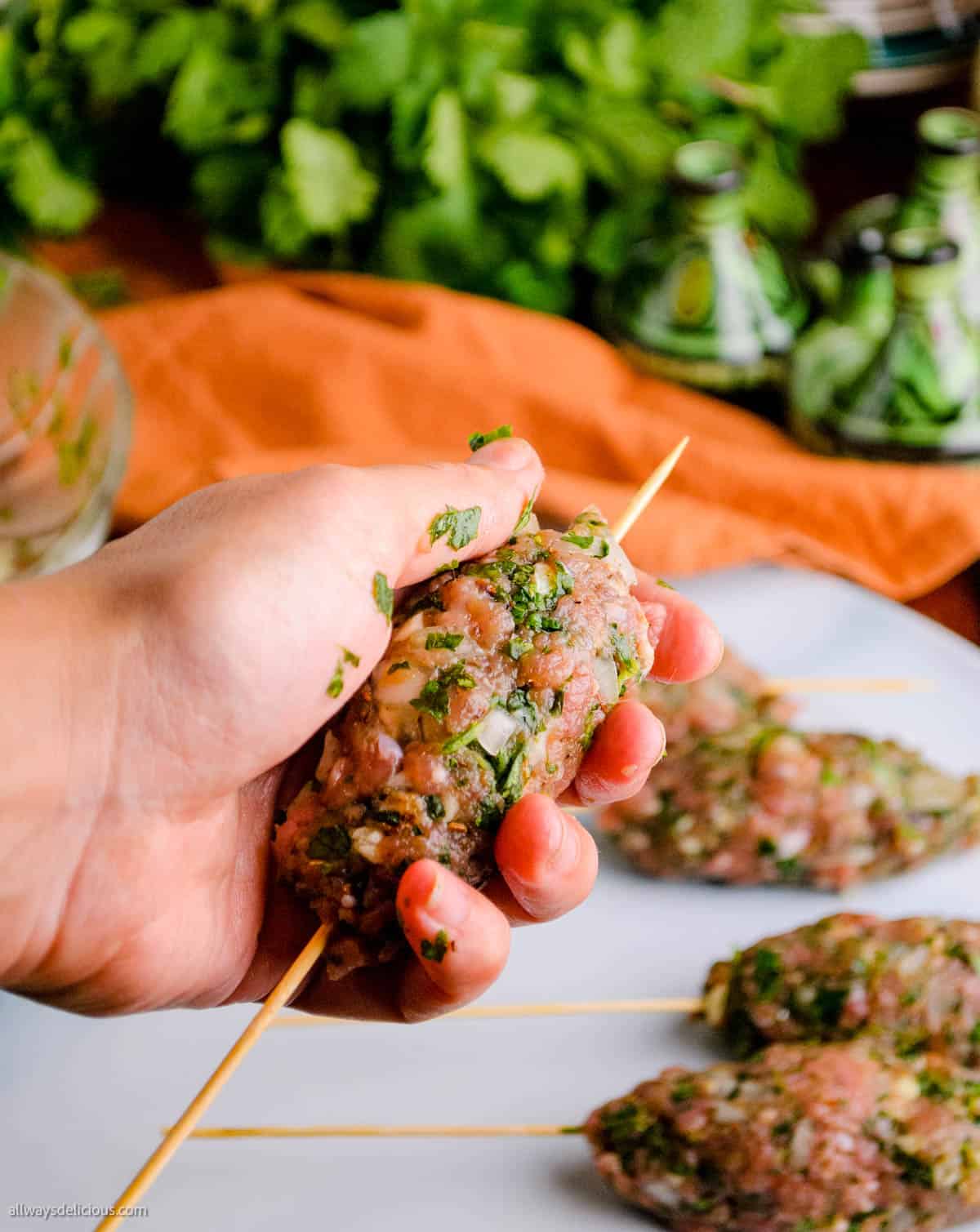 A person holding lamb kofta skewers on a plate.