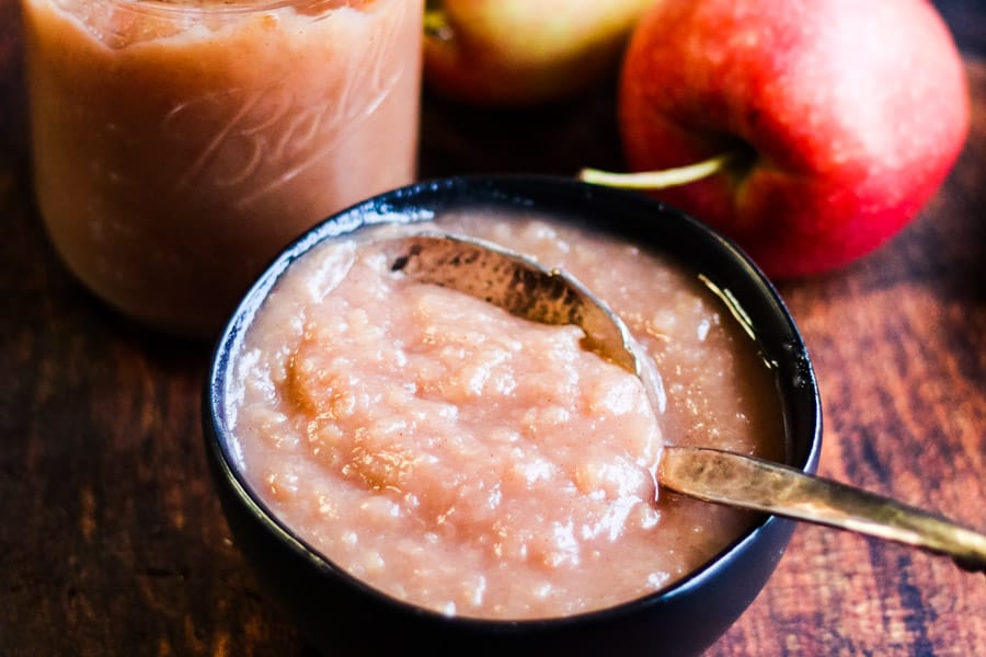 Instant pot applesauce in a bowl with a jar of appleasauce and some fresh apples