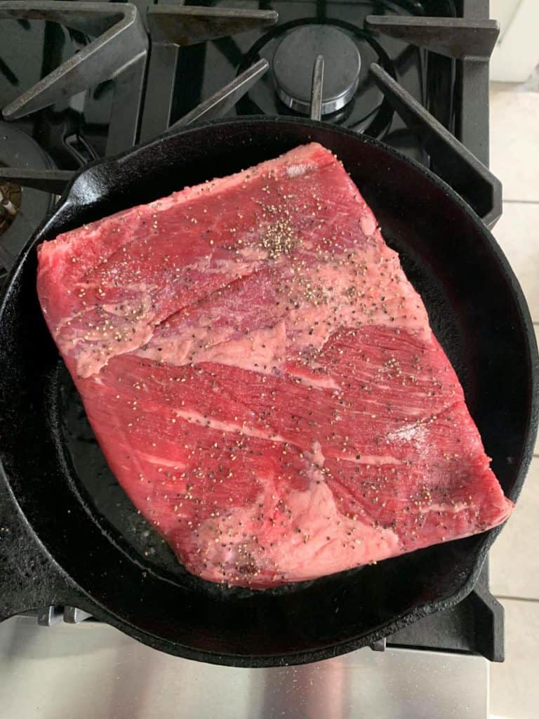 A beef steak is being cooked in a skillet on a stove using a flavorful brisket recipe.