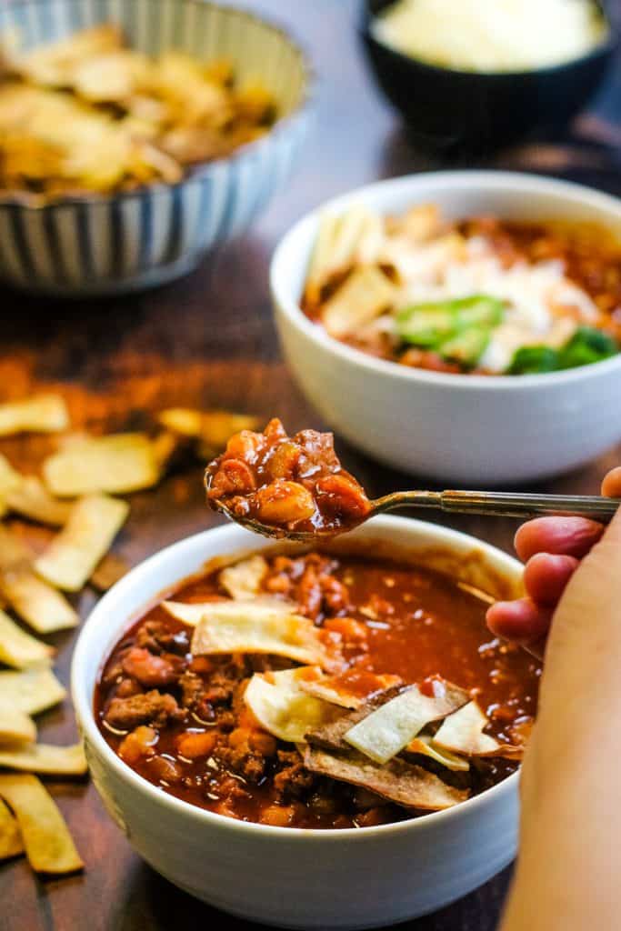 bowl of chili with a hand lifting a spoonful
