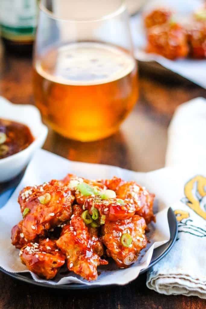 low angle shot of Korean chicken on a plate with a glass of beer