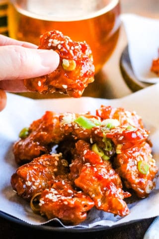 vetical shot of air fryer chicken in gochujang sauce with a hand lifting a piece