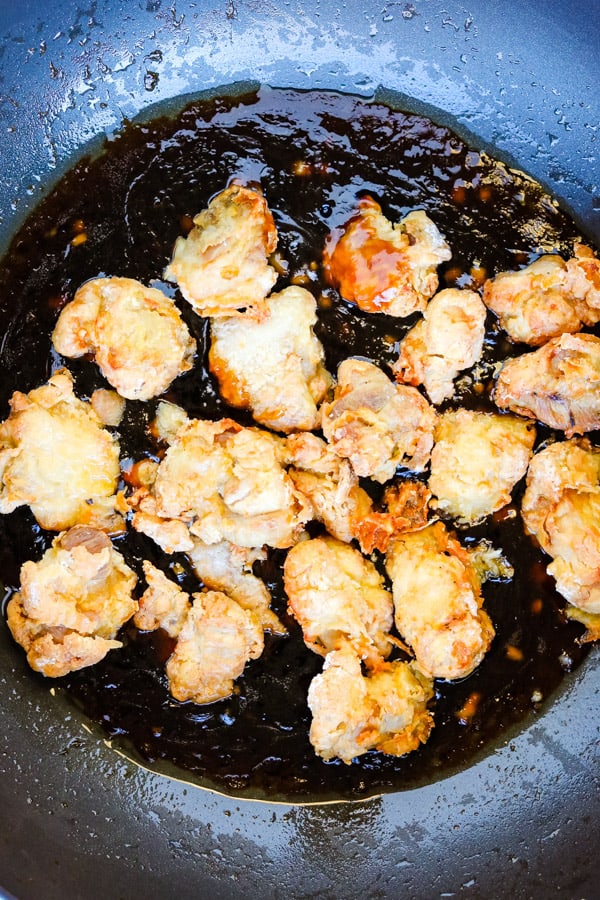 crispy chicken pieces added to sauce in pan
