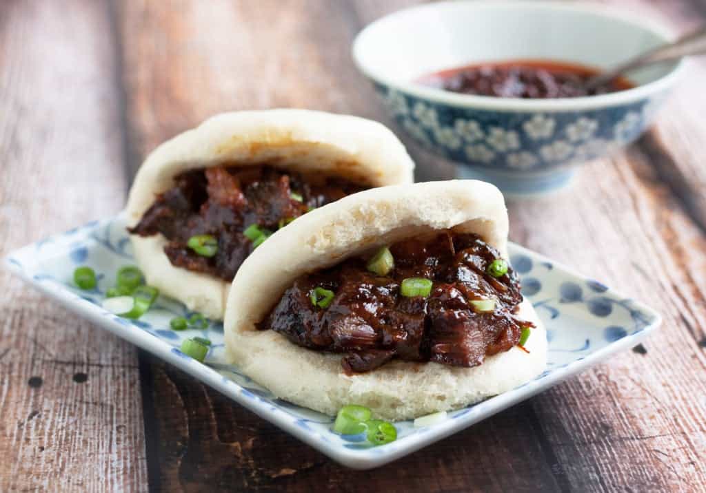 chinese steamed buns filled with char siu pork on a plate with scallion garnish
