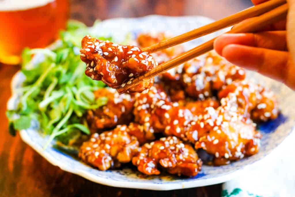 A person is holding chopsticks over a bowl of sesame chicken.