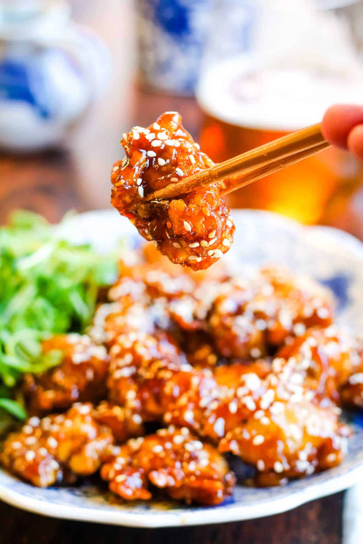 A person is holding chopsticks over a plate of sesame chicken.