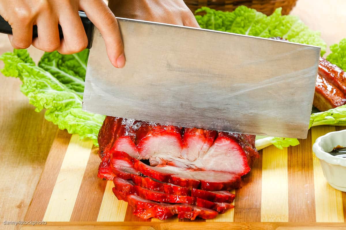 High angle shot of char siu being sliced with a cleaver.
