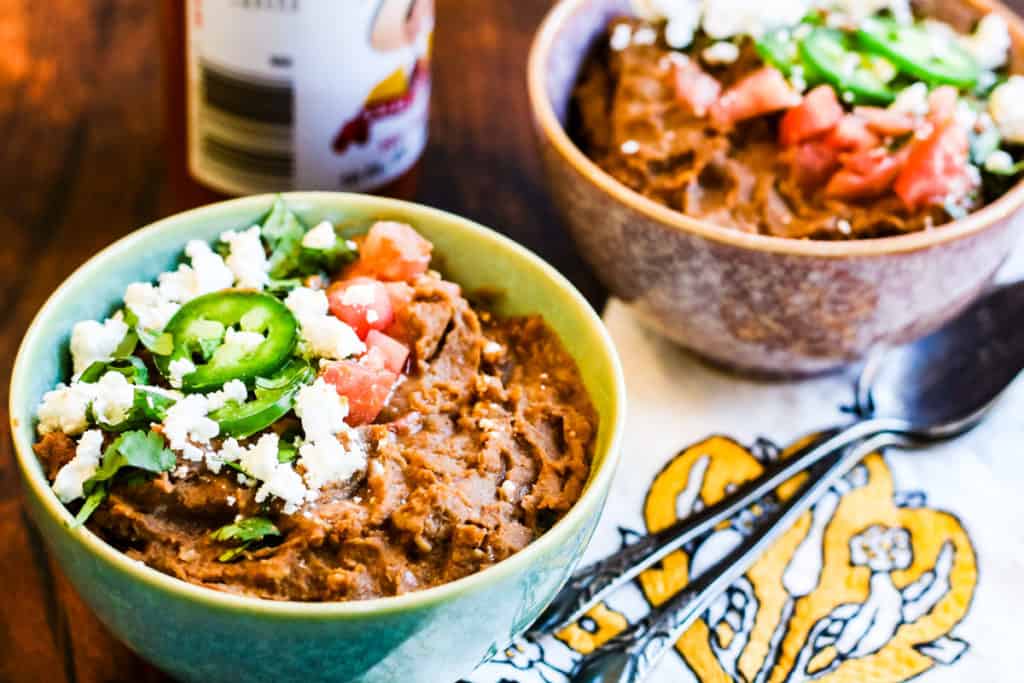 refried beans in bowls topped with cheese, sliced jalapeno, and tomatoes