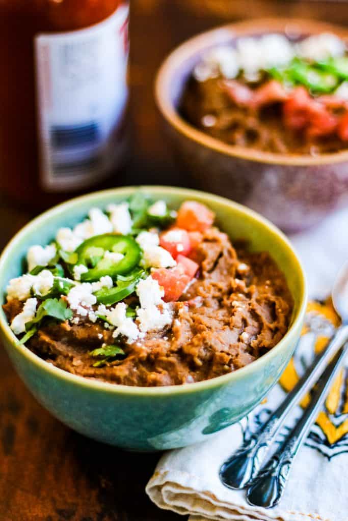 Two bowls of black bean soup with refried beans and guacamole.