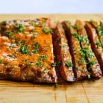 sliced grilled flank steak with chile butter melted on top. on a cutting board.