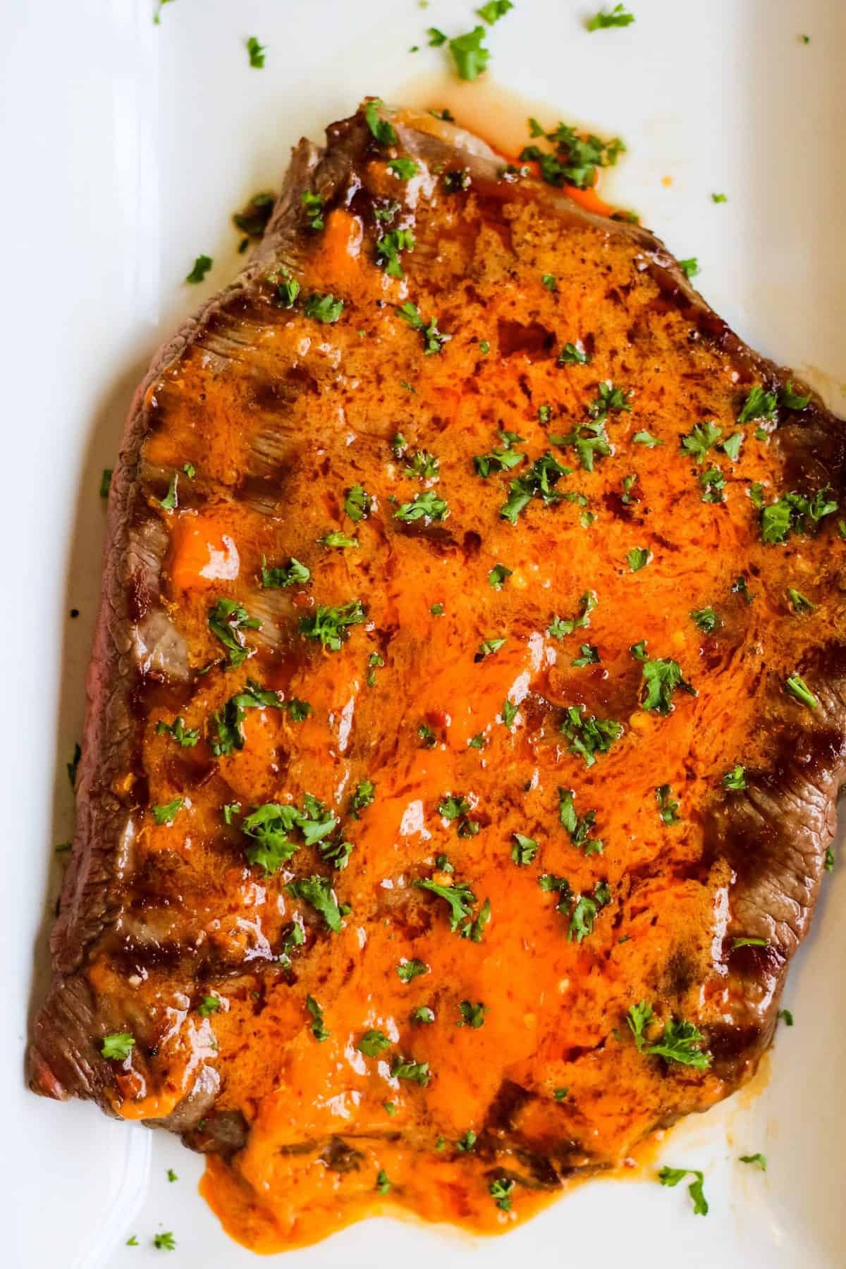 overhead shot of grilled flank steak with chile butter melted over the top. garnished with chopped parsley.