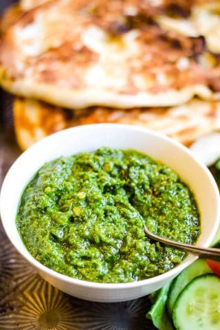 low angle shot of a bowl of the green zhoug sauce with flatbread in the background.