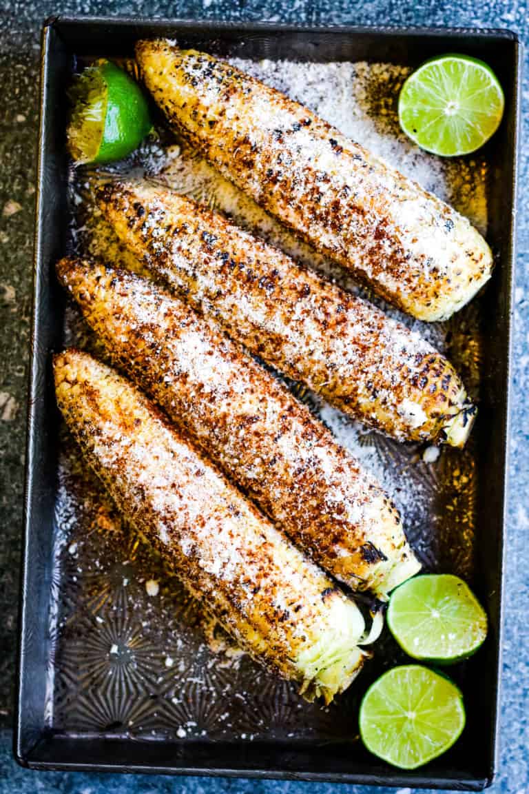 Overhead vertical shot of grilled Mexican corn with limes, cobs are coated with mayonnaise and sprinkled with chili powder and grated cheese