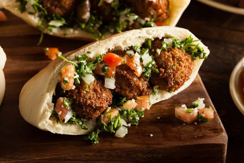 horizontal shot of of an instant pot falafel sandwich with three falafel balls, onions, tomatoes, and parsley in pita bread