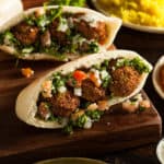low angle shot of falafel stuffed into pita bread with tahini and tomatoes.
