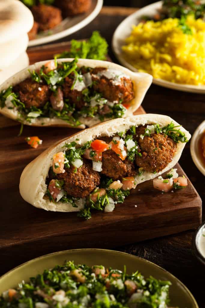 vertical shot of of an instant pot falafel sandwich with three falafel balls, onions, tomatoes, and parsley in pita bread