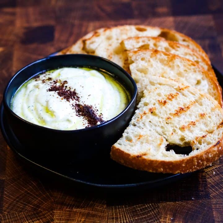 low angle shot of whipped feta dip in a black bowl with grilled sourdough bread